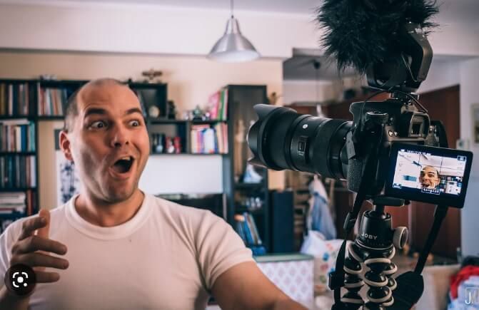 A Vlogging Man Wearing A White Round Neck Shirt Looks At This Camera. A vlogging man wearing a white round neck shirt looks at this camera.
